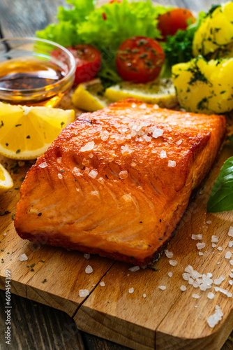 Seared salmon steak with lettuce, tomatoes and boiled potatoes on wooden table 
