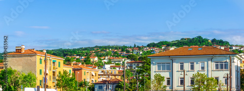 panoramic landscape view of green summer city with yellow houses, green forest and mountains above and amazing hills and cloudy sky on background