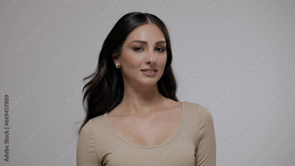 Young charming brunette woman with long wavy hair posing on a light gray background. Young charming brunette woman with long wavy hair posing on a light gray background.