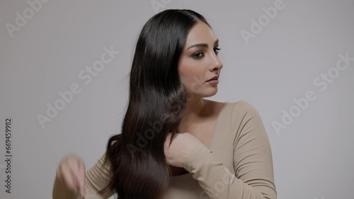 A young charming brunette woman combs her long wavy hair on a light gray background.