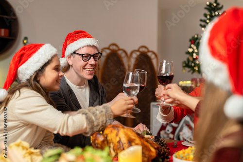 Happy family wearing Santa hats celebrating Christmas dinner and drinking cheer red wine together at home. Merry Christmas or New Year's eve concept