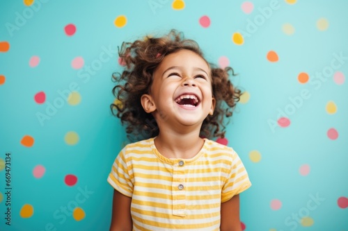 A girl in a striped t-shirt against a blue wall laughs and cheers.