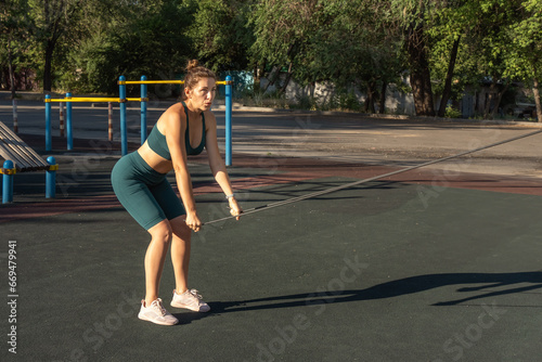 Young caucasian woman exercising with a rubber expander on a street sports ground