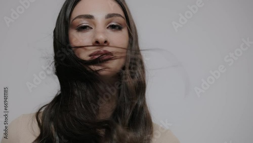 A young charming brunette woman with wind-blown hair posing on a light gray background.