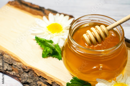 fresh honey in a jar on a wooden log with daisies. High quality photo