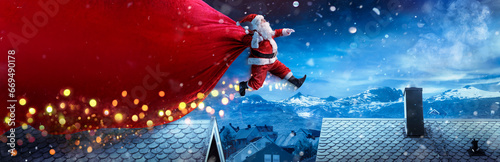 Santa Claus With Red Big Bag Jumping On Roofs In Snowy Winter Landscape - Fast Delivery Present