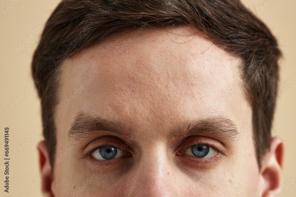 Close up macro shot of young man with striking blue eyes looking at camera against neutral background, copy space