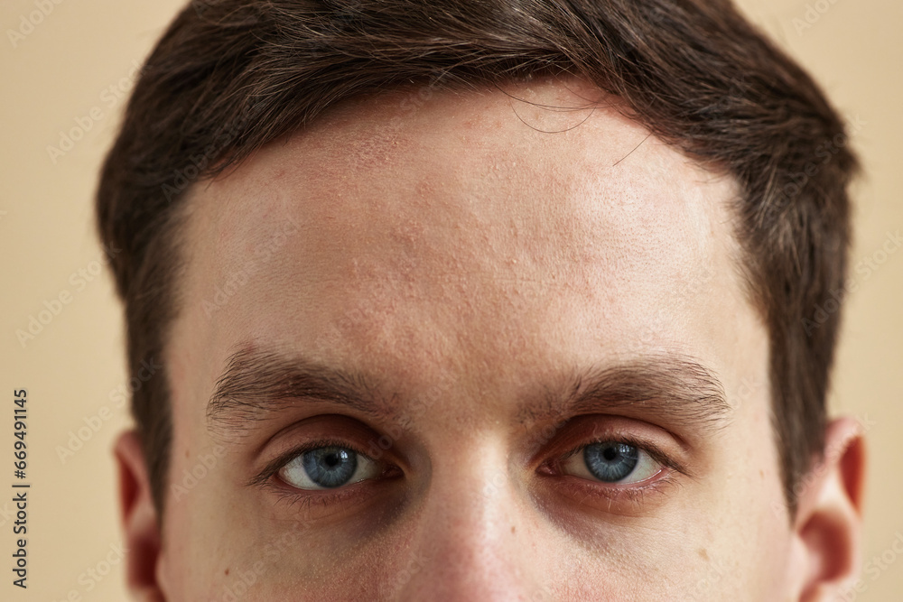 Close up macro shot of young man with striking blue eyes looking at camera against neutral background, copy space Close up macro shot of young man with striking blue eyes looking at camera against neutral background, copy space