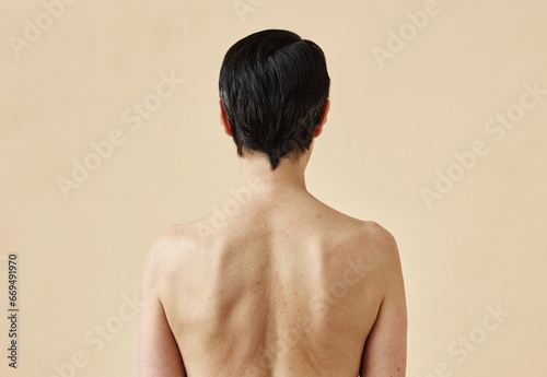 Rear view of unrecognizable adult woman with bare back standing against minimal beige background, copy space