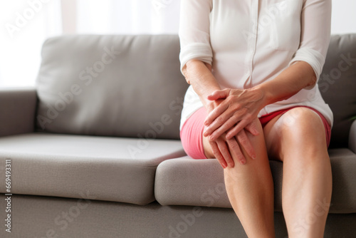 Senior woman suffering from knee ache sitting on sofa