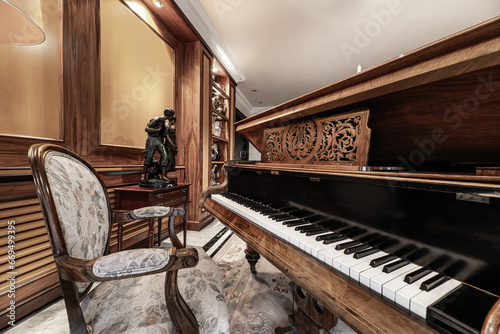Beautiful varnished wooden grand piano in a living room with saturated decoration, lots of wood on the walls, upholstered armchairs and Persian rugs on the floor © Toyakisfoto.photos
