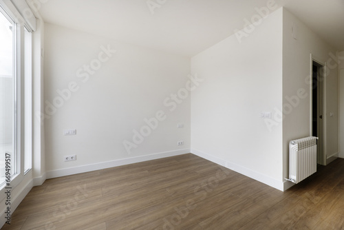 Empty room in a house with off-white painted walls, wooden floors and white aluminum radiators