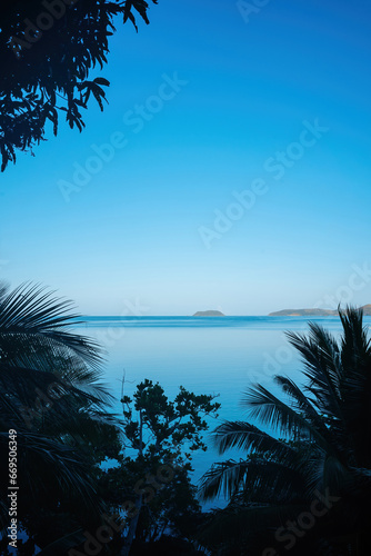 Silhouetted palms frame a calm, azure expanse, where distant islands nestle under a deep blue sky