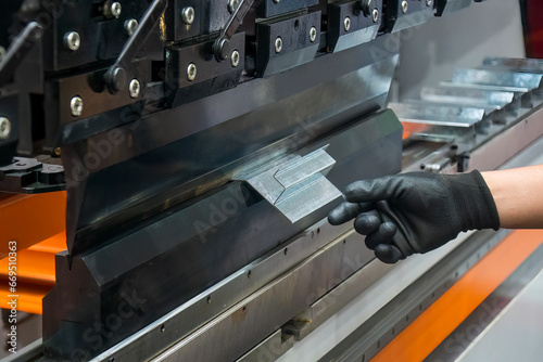 Close up the bending machine operator hold the sheet metal parts with rubber glove. photo