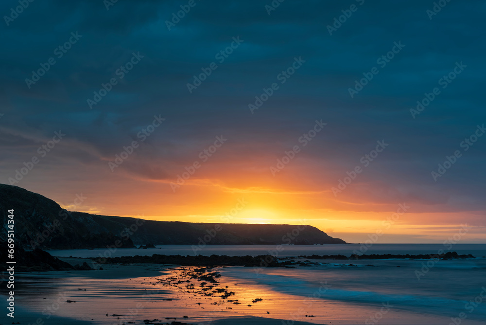 Beautiful sunrise landscape image of Kennack Sands in Cornwall UK wuth dramatic moody clouds and vibrant sunburst