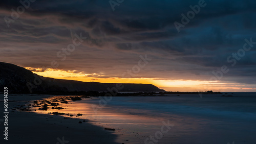 Beautiful sunrise landscape image of Kennack Sands in Cornwall UK wuth dramatic moody clouds and vibrant sunburst