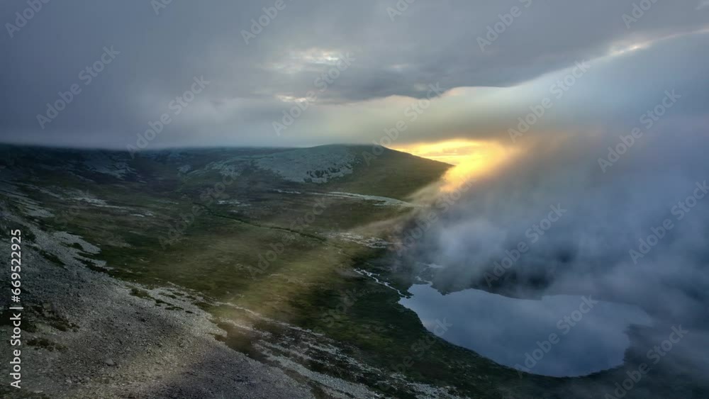 Aerial drone shot of sunrise in the mountains, fiery yellow sun rays breaking through the fog and white clouds. Flying over tundra landscape with mountain river and lake, Swedish wilderness Aerial drone shot of sunrise in the mountains, fiery yellow sun rays breaking through the fog and white clouds. Flying over tundra landscape with mountain river and lake, Swedish wilderness