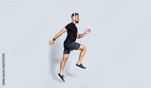 Focused millennial european guy in wireless headphones, sportswear listen music, run