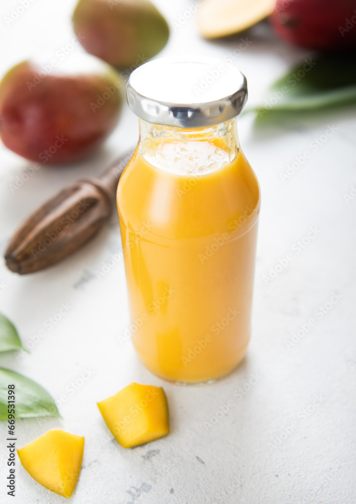 Bottle of fresh mango smoothie with pieces on light background.