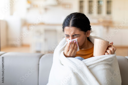 Cold And Flu Symptoms . Sick indian woman covered in blanket blowing nose photo