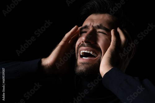Stressed Young hopeless man screaming and shouting Frustrated handsome man agonizing and torturing expression He get maddening and overwhelming rage in the dark room black background Agressive man photo