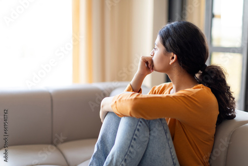 Portrait Of Pensive Depressed Young Indian Woman Sitting On Couch At Home