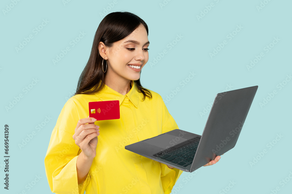 Obraz premium Beautiful young woman holding credit card and laptop