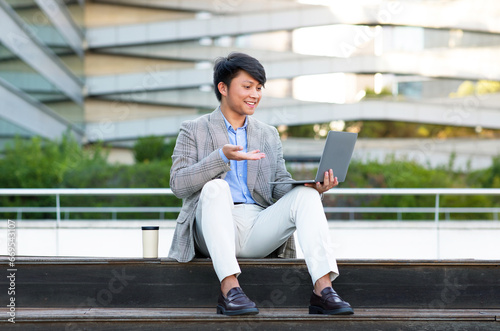 Asian businessman conducting an online meeting via laptop sitting outdoors
