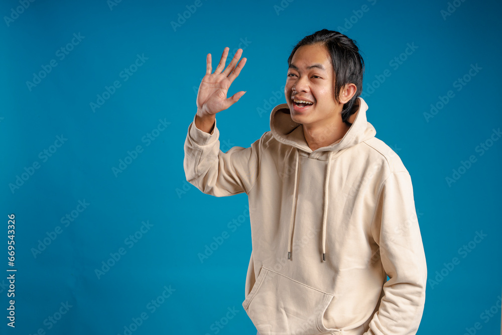 A man wearing a hoodie jacket waved his hand as if to say hello. A man wearing a hoodie jacket waved his hand as if to say hello.