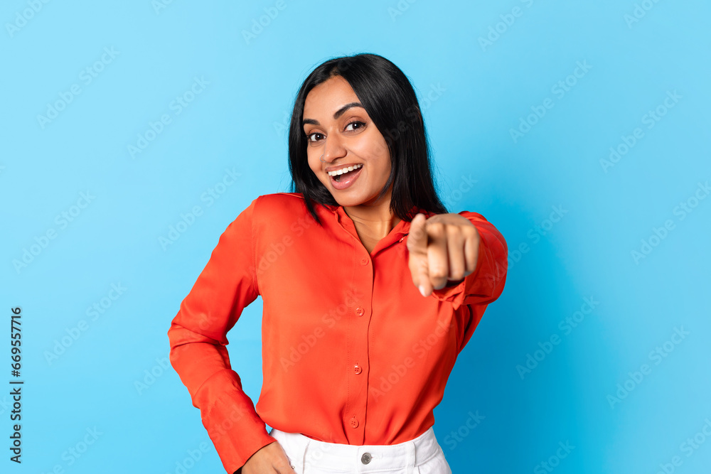 Smiling hindu lady against blue background pointing finger at camera Smiling hindu lady against blue background pointing finger at camera