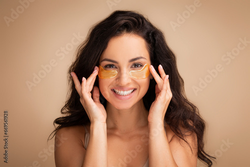 Smiling young brunette woman applying golden patches under eyes photo