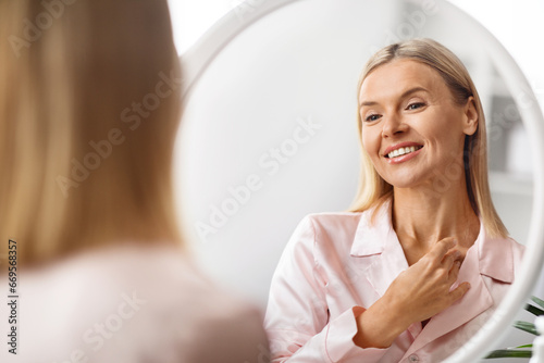 Middle Aged Woman Touching Soft Skin On Neck While Looking In Mirror photo