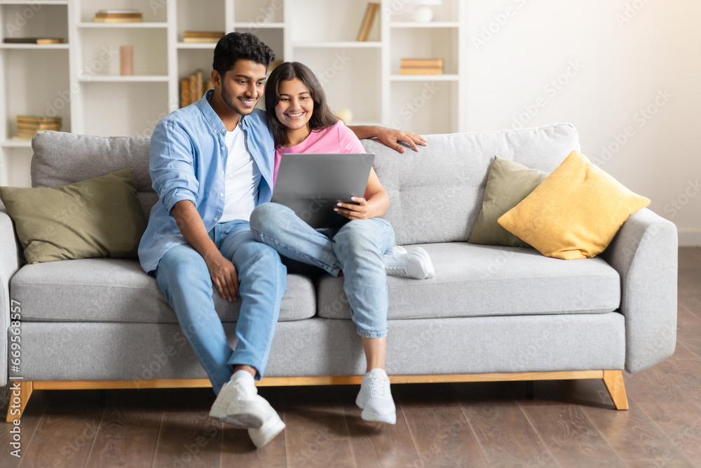 Happy Indian couple on sofa, using laptop computer together, free space Happy Indian couple on sofa, using laptop computer together, free space