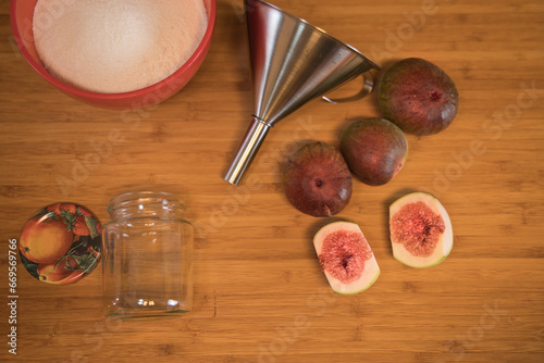 Figs, sugar, a jar with a lid and a funnel for preparing the jam on a wooden board