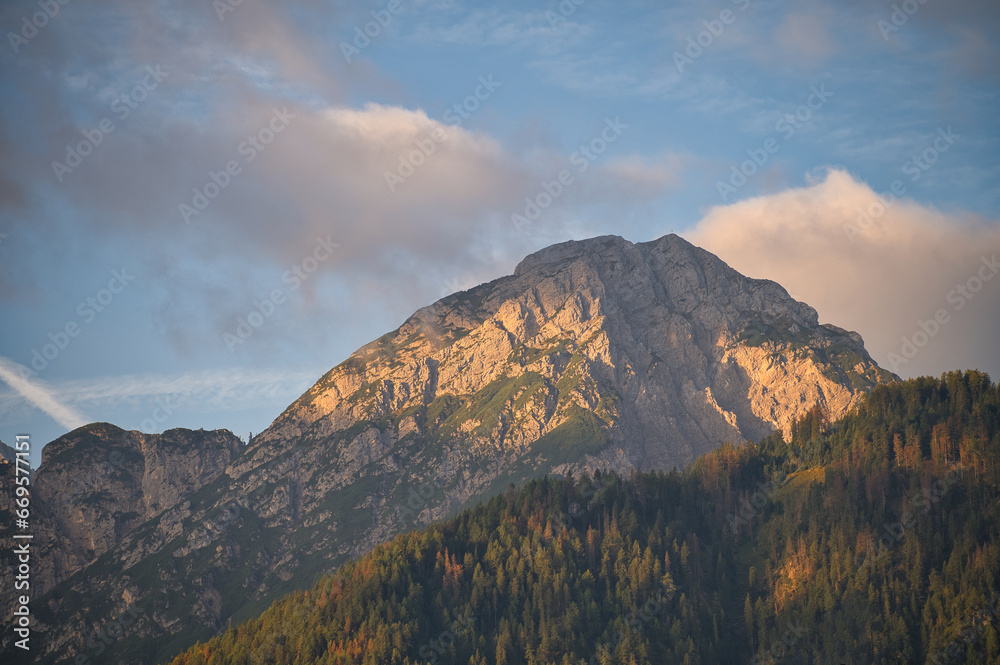 Ein Bergmassiv in Südtirol bei Sonnenaufgang im goldenen Licht umgeben von einem Wald