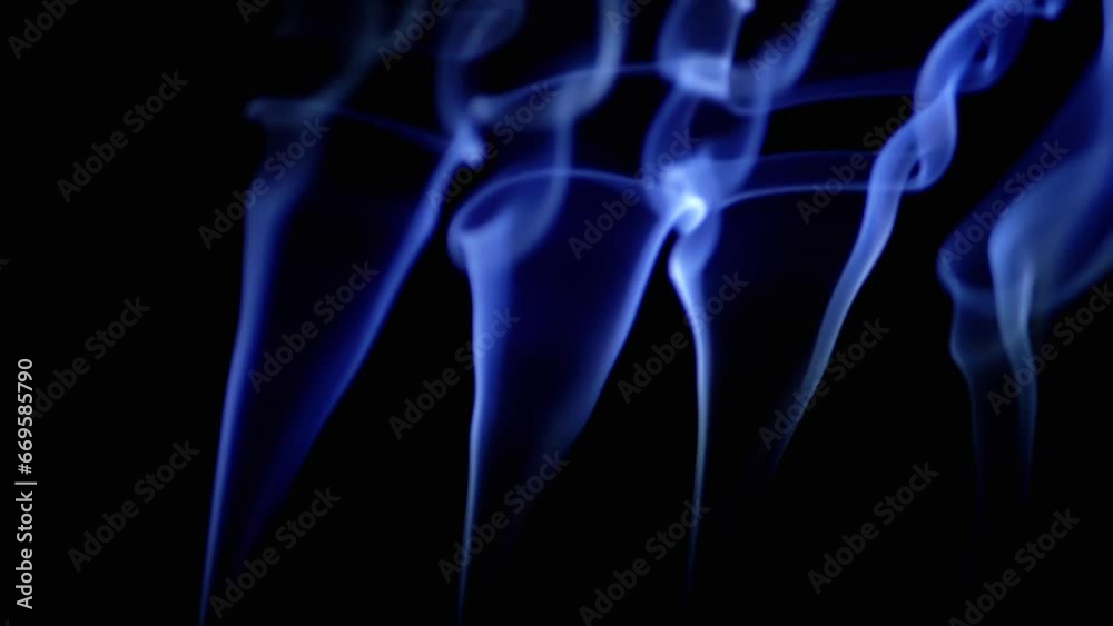Thin Curls of Blue Smoke Rise Up, Fill Empty Space on a Black Background. Incense sticks. Abstract shapes. Texture. Beautiful clouds of smoke swirl. Floating fog, flowing smoke. Blurred motion. Light.