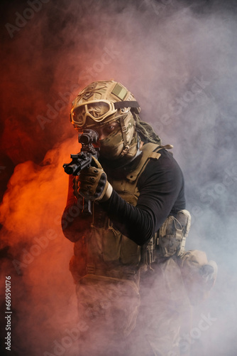 A soldier in combat gear with a weapon in his hands stands in battle formation among fire and smoke. The concept of military affairs. Computer games. The concept of war and combat.