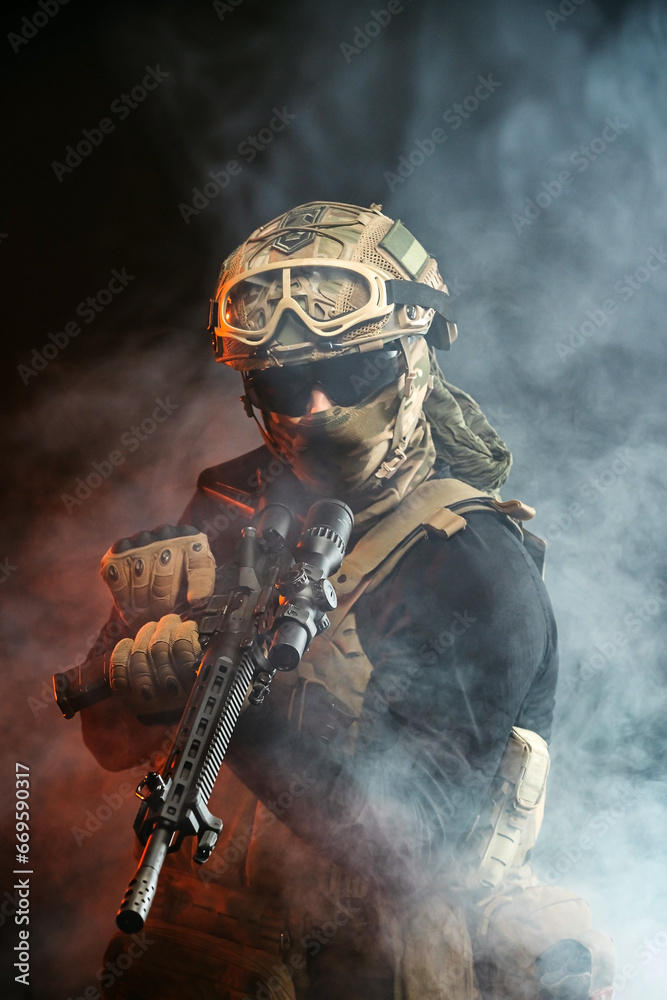 Fototapeta premium A soldier in combat gear with a weapon in his hands stands in battle formation among fire and smoke. The concept of military affairs. Computer games. The concept of war and combat.