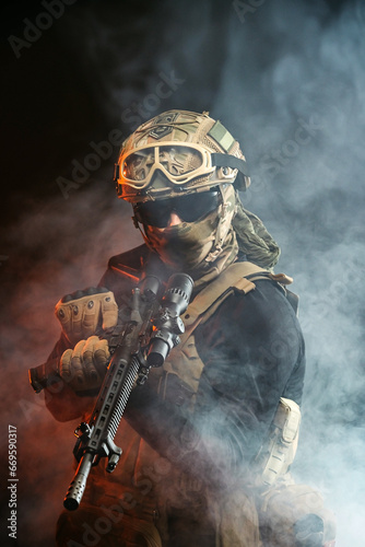 A soldier in combat gear with a weapon in his hands stands in battle formation among fire and smoke. The concept of military affairs. Computer games. The concept of war and combat.
