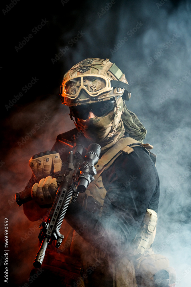 A soldier in combat gear with a weapon in his hands stands in battle formation among fire and smoke. The concept of military affairs. Computer games. The concept of war and combat. A soldier in combat gear with a weapon in his hands stands in battle formation among fire and smoke. The concept of military affairs. Computer games. The concept of war and combat.