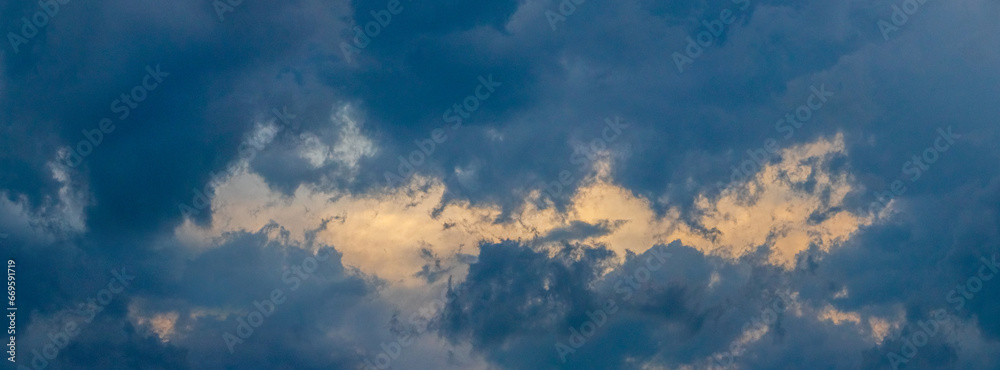 A patch of sky illuminated by the evening sun shines through the dark blue clouds