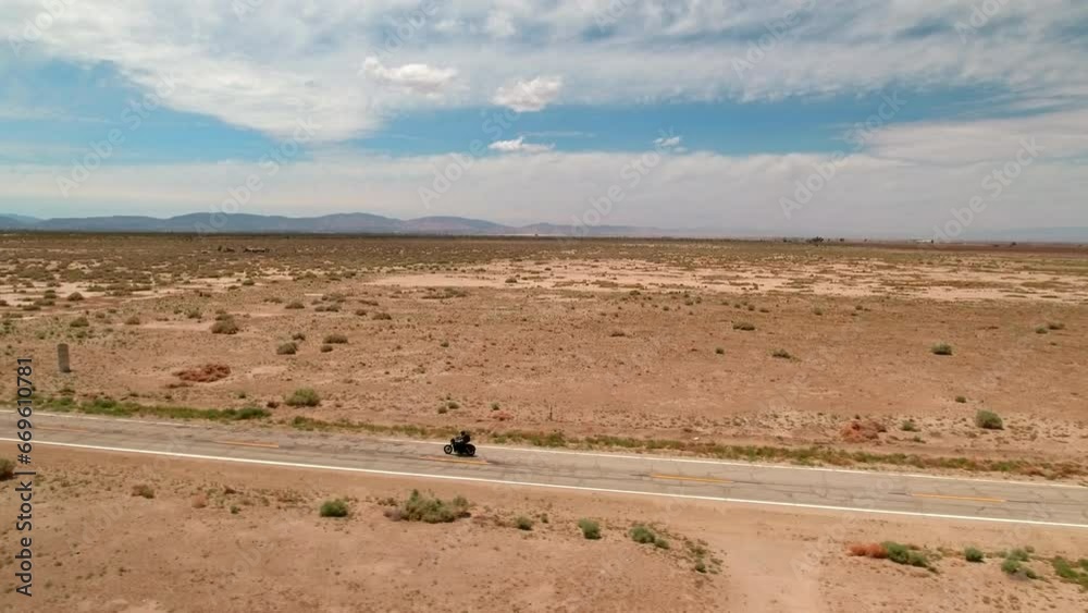 Aerial Panning Shot Of Man Riding Motorcycle Near Mountains In Desert Against Sky - Landers, California Aerial Panning Shot Of Man Riding Motorcycle Near Mountains In Desert Against Sky - Landers, California