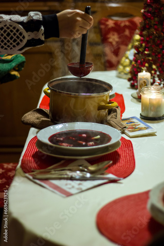 A woman hand is taking out hot beetroot soup from a pot and serving it on a plate, easter or xmas holiday celebration concept