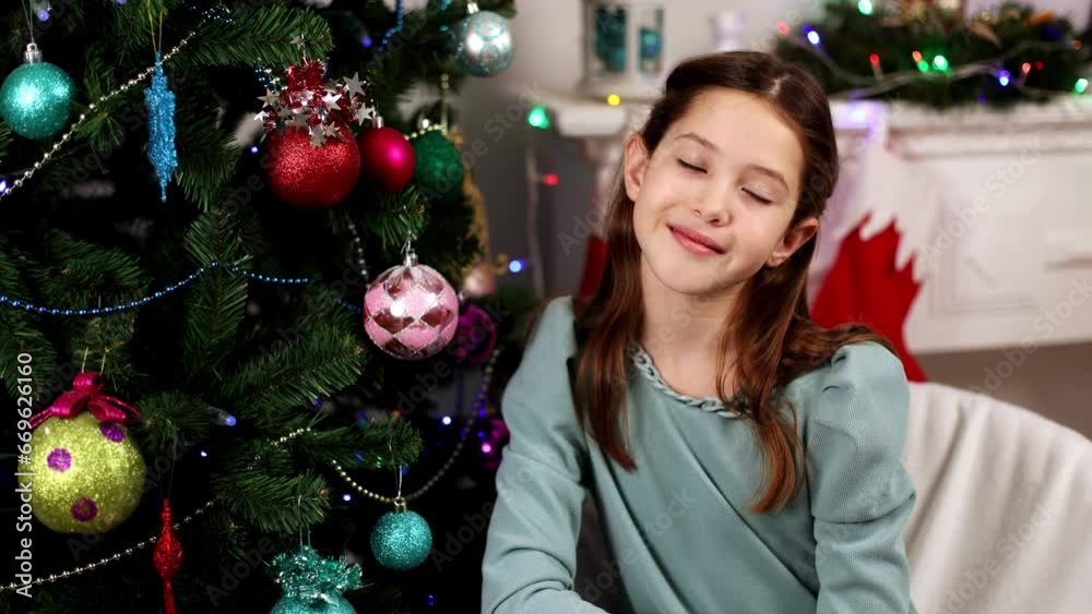 Cute teenage girl sitting in an armchair in her room next to the Christmas tree, copy space Cute teenage girl sitting in an armchair in her room next to the Christmas tree, copy space