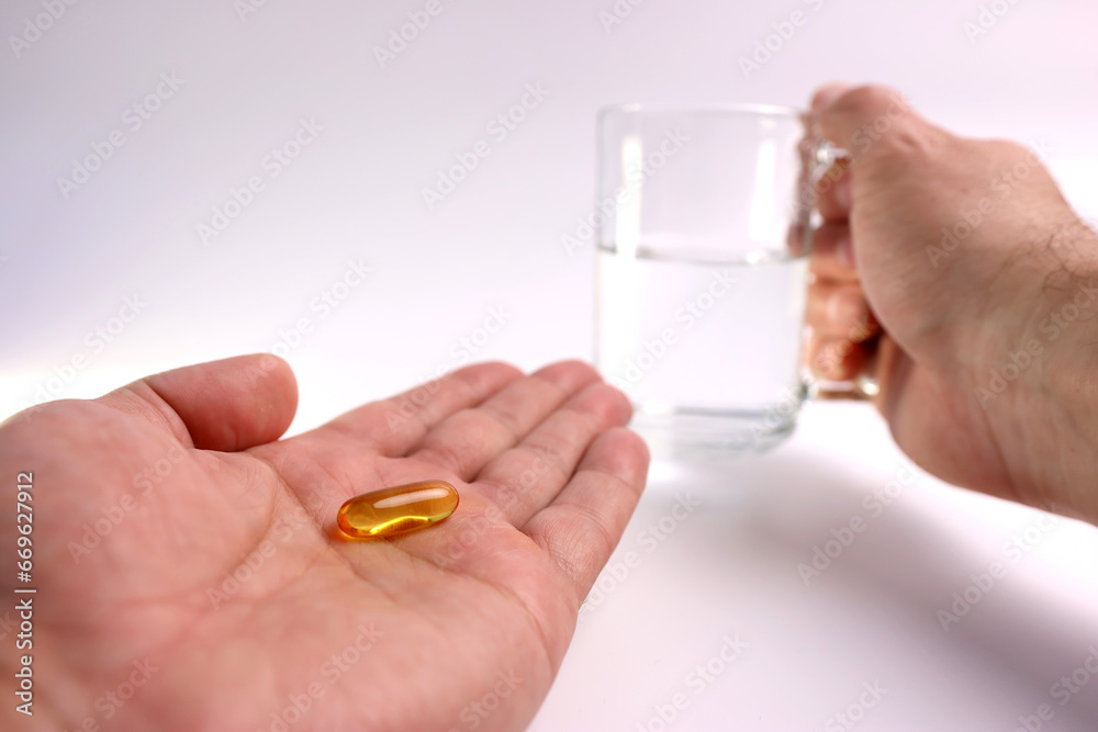 A man holds a polyunsaturated fatty acid complex capsule in his hand. Prevention and treatment of ischemic heart disease, atherosclerosis of cerebral vessels. A man holds a polyunsaturated fatty acid complex capsule in his hand. Prevention and treatment of ischemic heart disease, atherosclerosis of cerebral vessels.