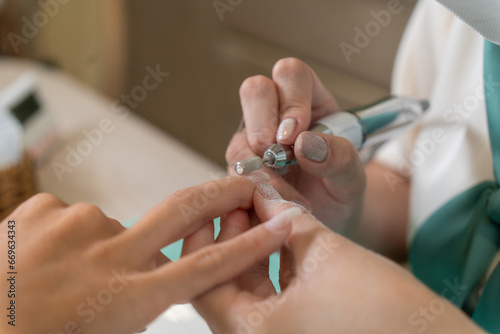 close up of beautician with electric nail drill in beauty manicure salon. Nail manicure treatment with electric machine