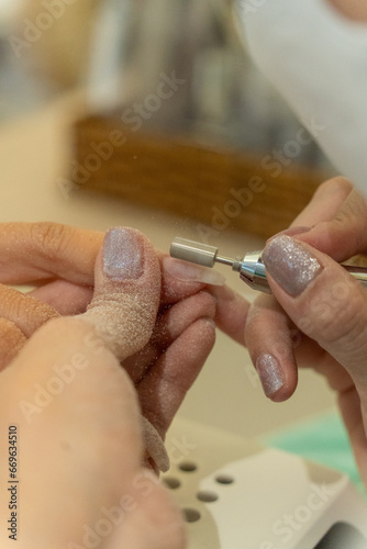 close up of beautician with electric nail drill in beauty manicure salon. Nail manicure treatment with electric machine