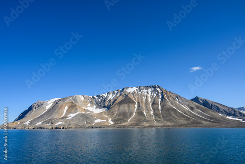 Peaceful sunny blue landscape of arctic ocean, rocky mountain range with snow, and blue sky, Gashamna, Svalbard
