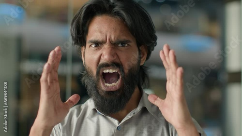 Close-up emotional angry aggressive furious displeased stressful irritated mad Indian bearded man guy shouting screaming yelling swearing shout scream looking at camera stressed male portrait indoors photo