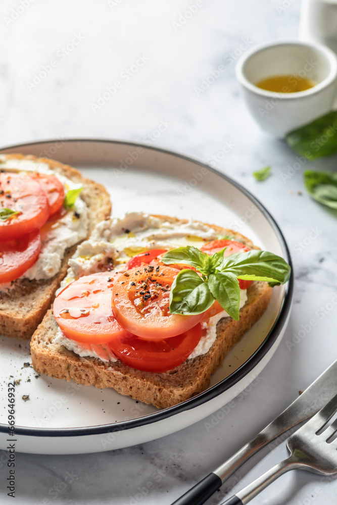 Sandwiches or toasts with tomatoes, cream cheese, olive oil and basil on a plate on white marble background. Traditional italian mediterranean food Sandwiches or toasts with tomatoes, cream cheese, olive oil and basil on a plate on white marble background. Traditional italian mediterranean food